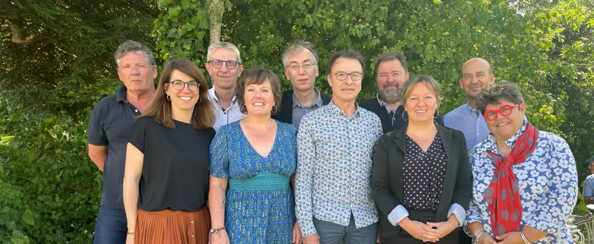 Groupe de neuf personnes posant ensemble en extérieur devant des arbres, souriantes et alignées pour une photo.