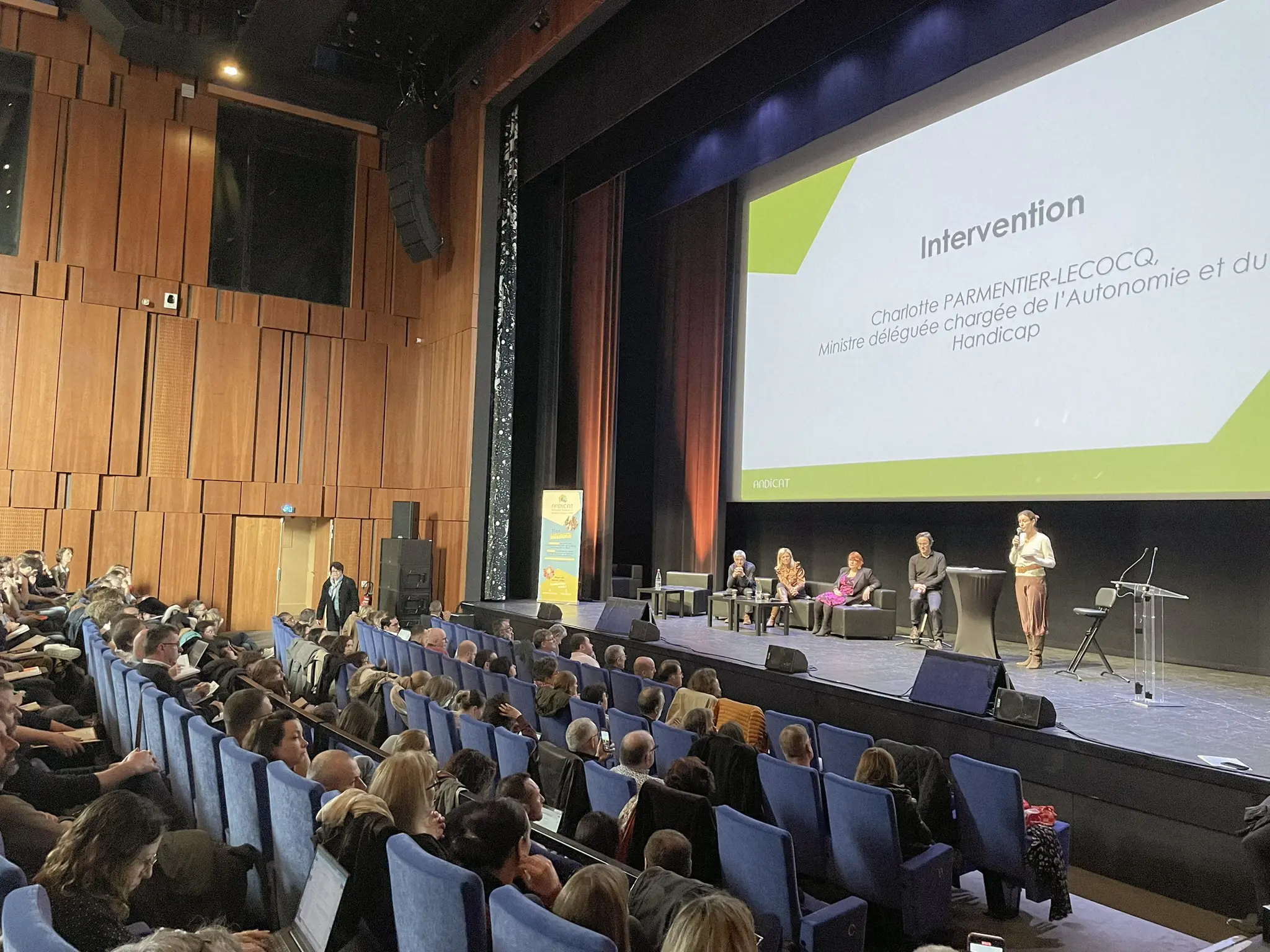 Conférence ANDICAT dans un auditorium, intervenants sur scène face à un public nombreux.